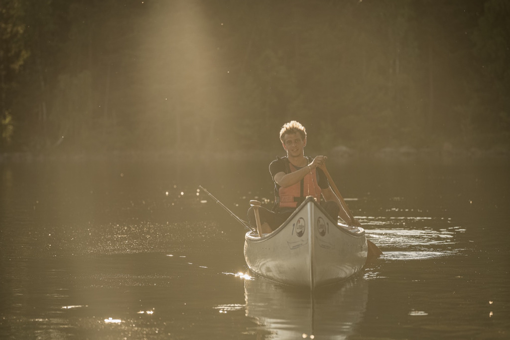 Ein Paddler sitzt alleine in einem Kanu und fährt durch das goldene Licht eines späten Nachmittags in Südschweden.